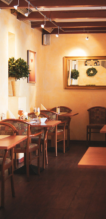 Das einladende Interieur eines rustikalen Restaurants mit warmer Beleuchtung, Holztischen und Stühlen mit gemusterten Polstern. An einer gelben Wand hängt ein großes Gemälde, das einen Stier zeigt, und ein quer hängender Spiegel spiegelt den Speisesaal wider.